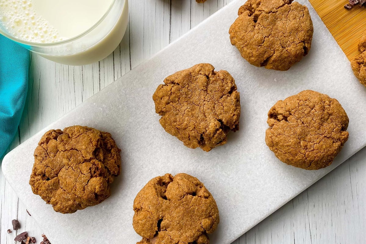 Glass of milk next to six chocolate chip cookies on a white marble board