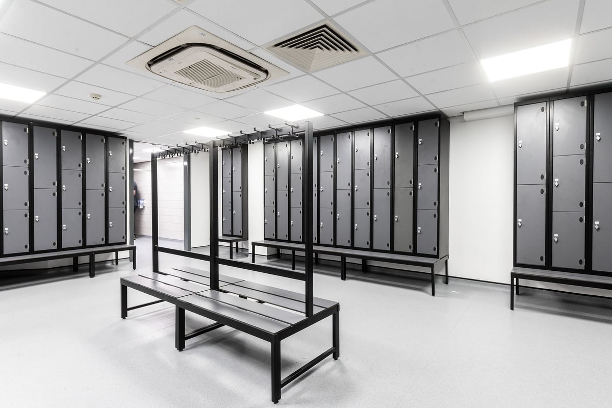 PureGym Aintree: Rows of lockers, benches, and an air conditioning unit in a utilitarian space.