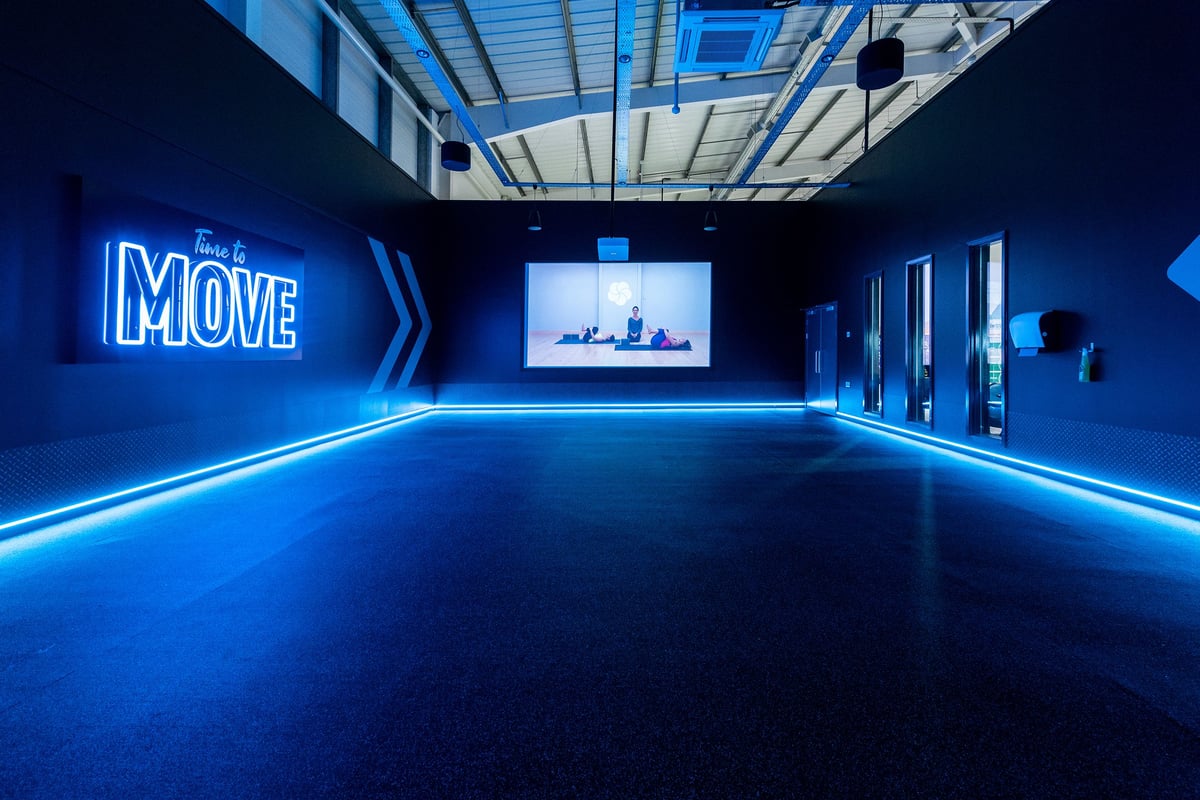 PureGym Torquay Bridge Retail Park: A futuristic studio with neon "Move" signage, a large screen, and blue accent lighting.