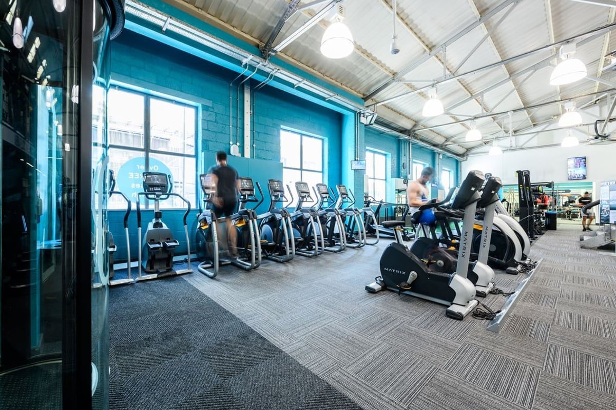 PureGym London Clapham: Rows of cardio machines in a bright space with teal accents and exposed ceiling structure.