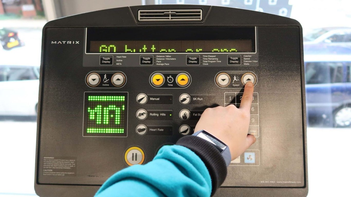Hand pressing speed increase button on treadmill control panel with digital display