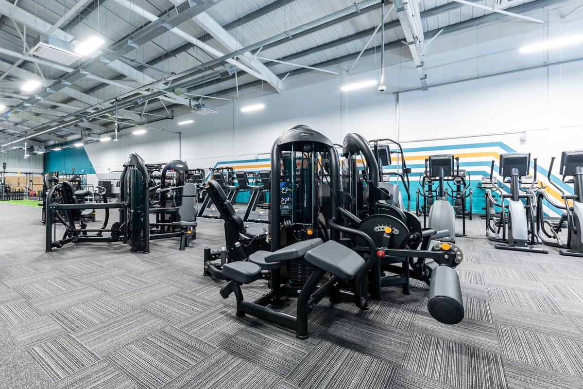 PureGym Byfleet: Rows of resistance machines, weight stacks, benches, and rubber flooring in a large gym space.