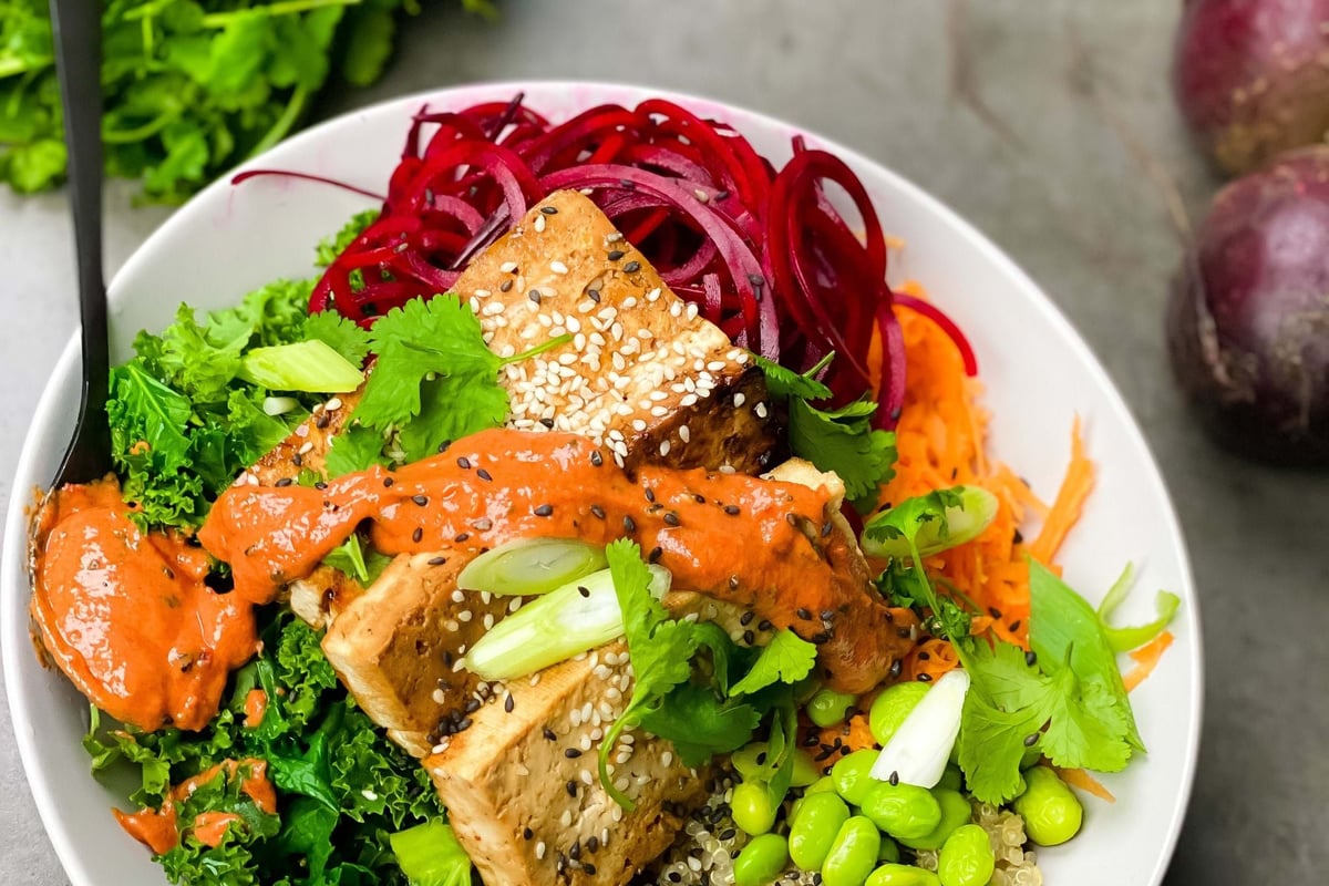 Bowl with tofu, quinoa, kale, edamame, shredded carrot, beet spirals, and sauce