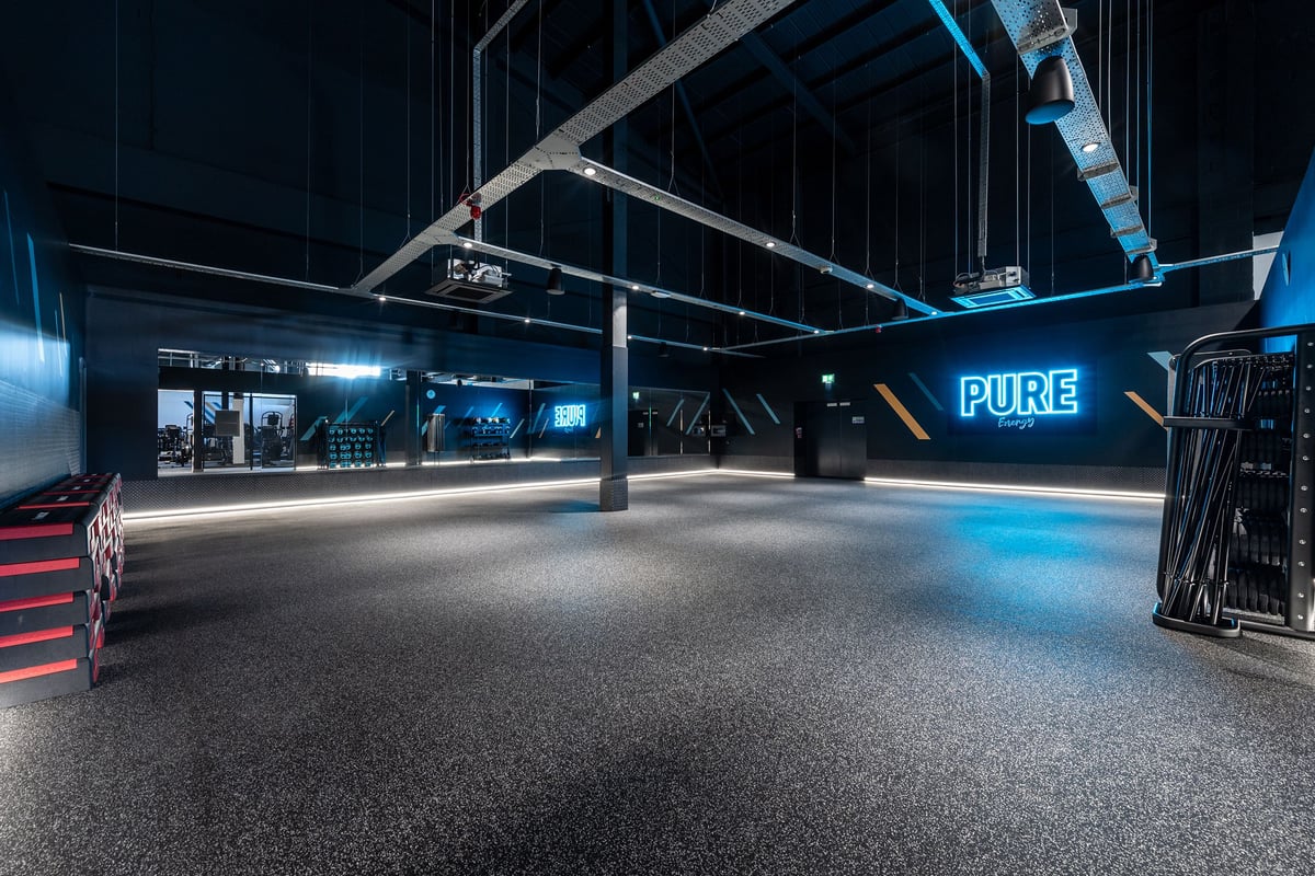 PureGym Stockton-on-tees Teesside Park: Studio with weights, benches, mirrors, neon lighting, and rubberized flooring.