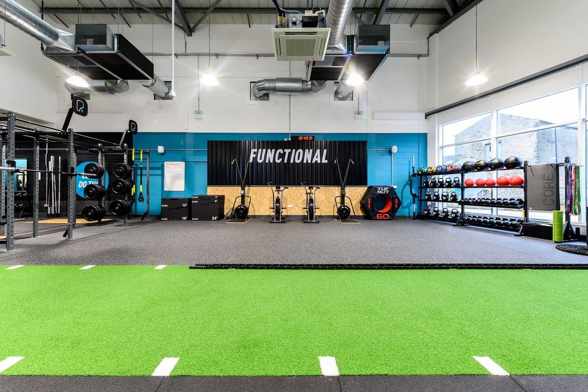 PureGym Glossop: Functional training area with squat racks, weight plates, turf zone, and rubberized flooring.