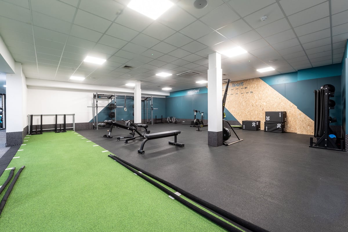 PureGym Harlow: Green turf area, weight benches, mirrored wall, exercise machines, rubberized flooring.