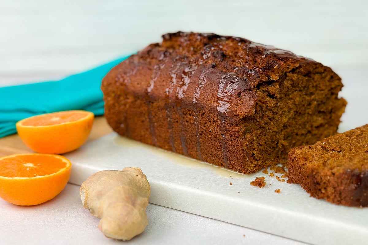 Sliced gingerbread loaf on white board with orange halves and ginger root