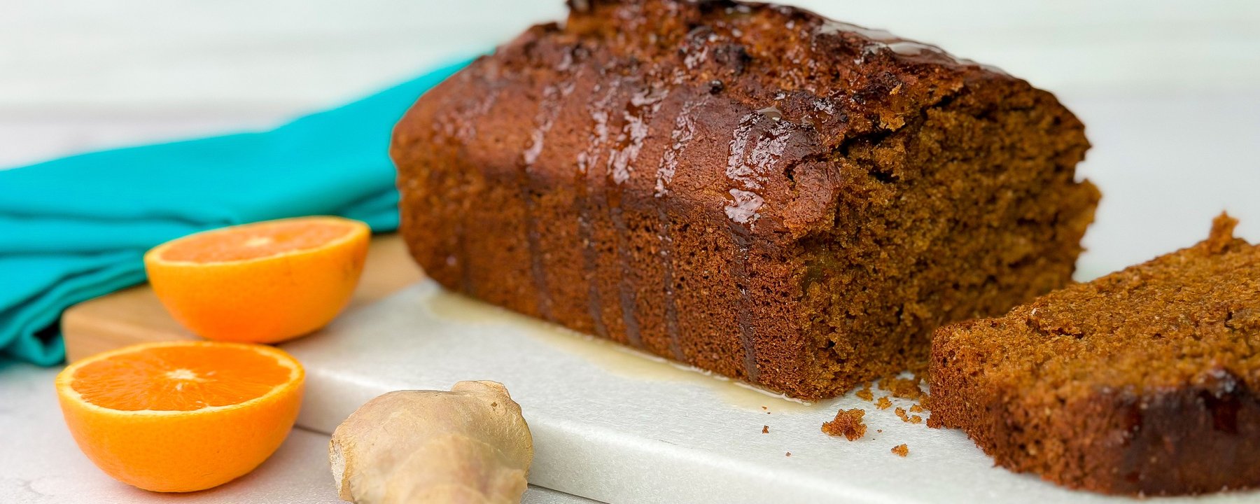 Sliced gingerbread loaf on white board with orange halves and ginger root
