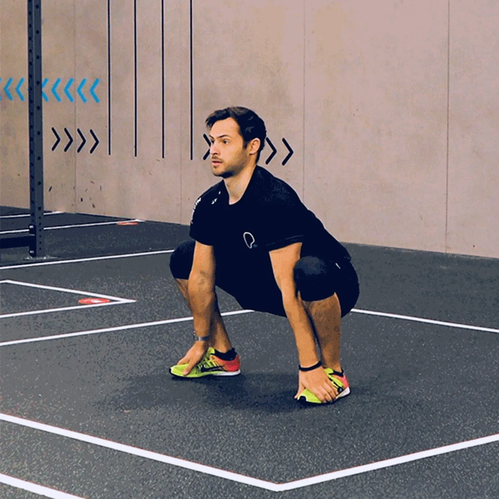 Man in black sportswear performing deep squat on gym floor with yellow trainers