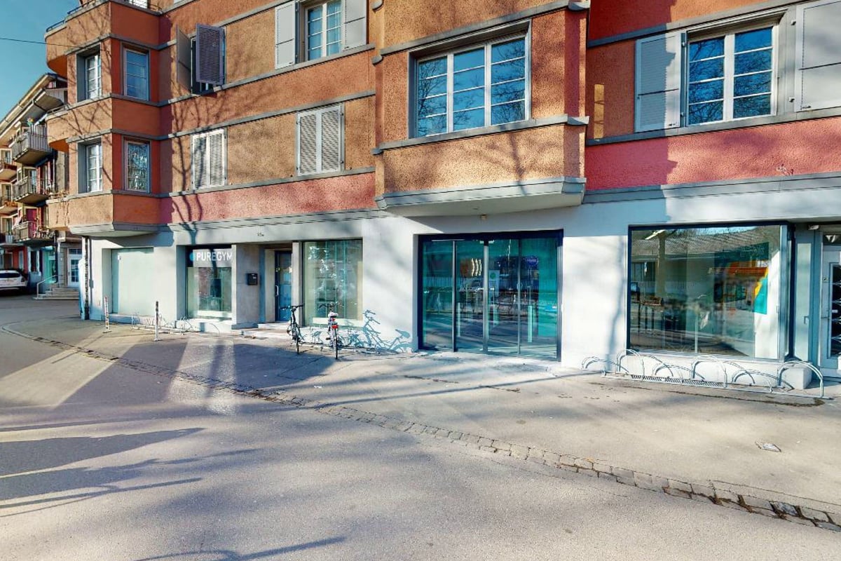 PureGym Bern Lorraine: Extérieurs en vitrine avec vélos garés à l'extérieur, bancs et espaces commerciaux vides.