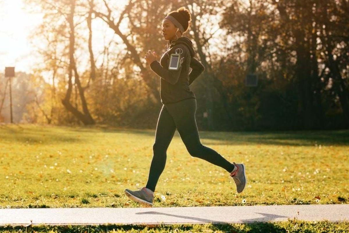 Woman jogging on a path in a park with autumn trees and sunlight in the background