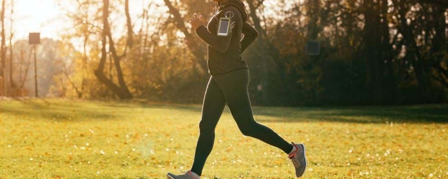 Woman jogging on a path in a park with autumn trees and sunlight in the background