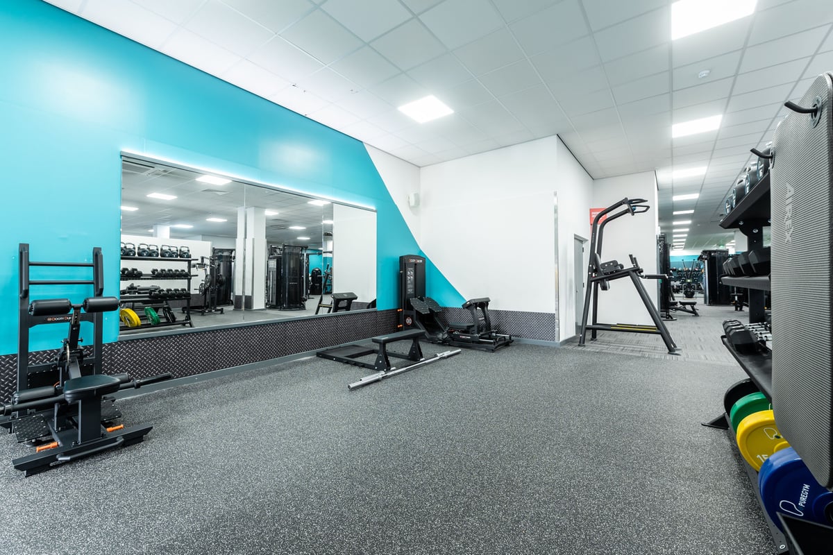 PureGym London Ilford: Gym area with resistance machines, sled rails, weight racks, rubberized floors, and teal accent walls.