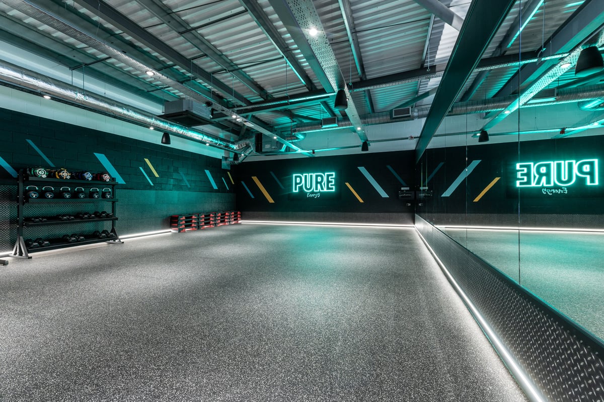 PureGym Plymouth Derriford: Teal-lit studio with wall branding, flooring for functional training, and equipment racks.