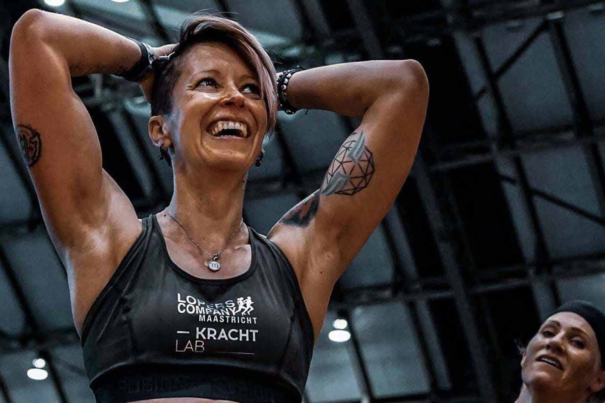 Frau in schwarzem Sporttop mit Händen hinter dem Kopf, lächelnd während des Trainings in e