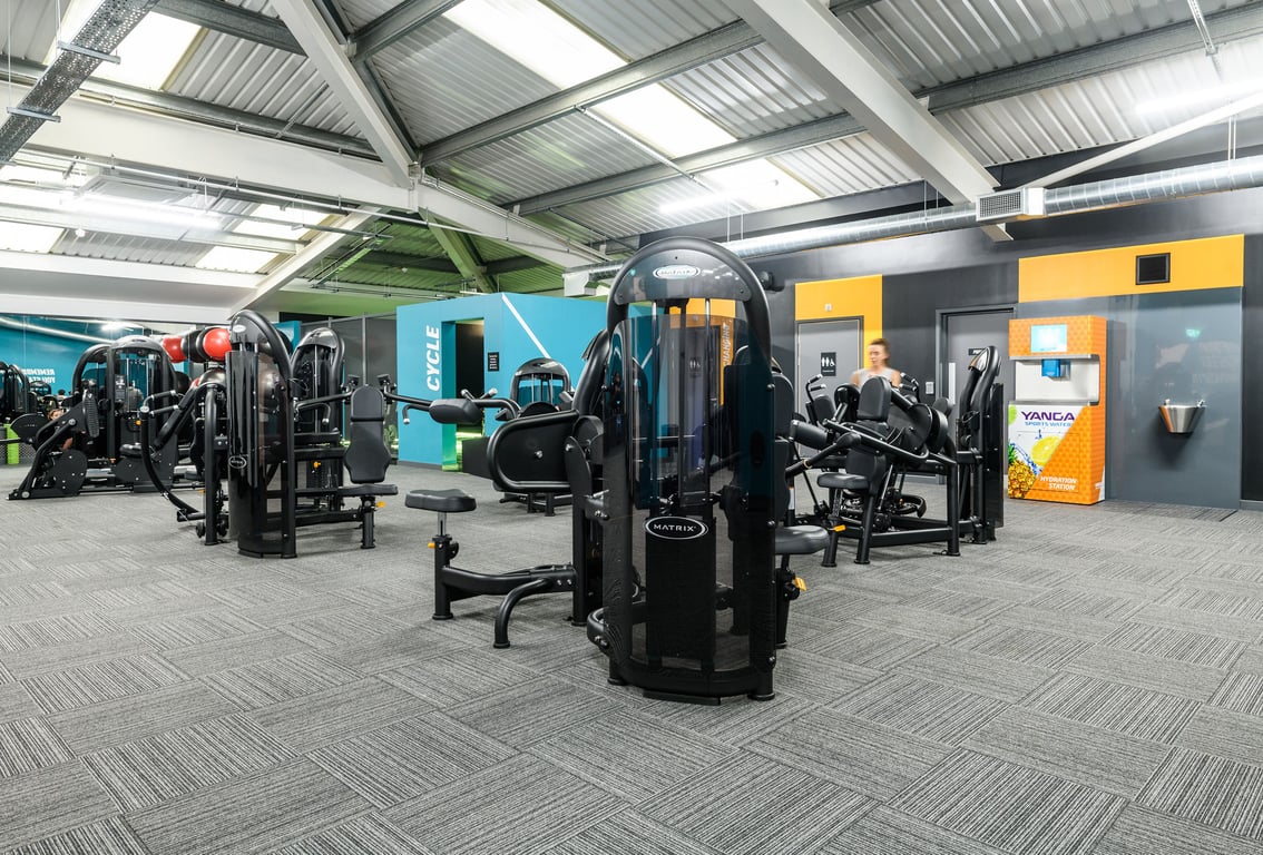 PureGym Bletchley: Resistance machines, weight racks, benches, mirrors, and rubberized flooring in a gym facility.