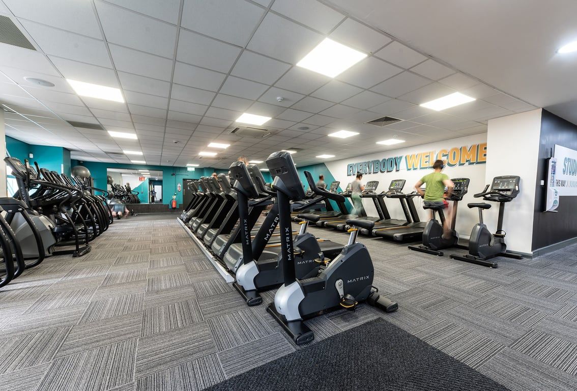 PureGym Woking: Rows of exercise bikes, ellipticals and treadmills in a brightly lit fitness centre interior.
