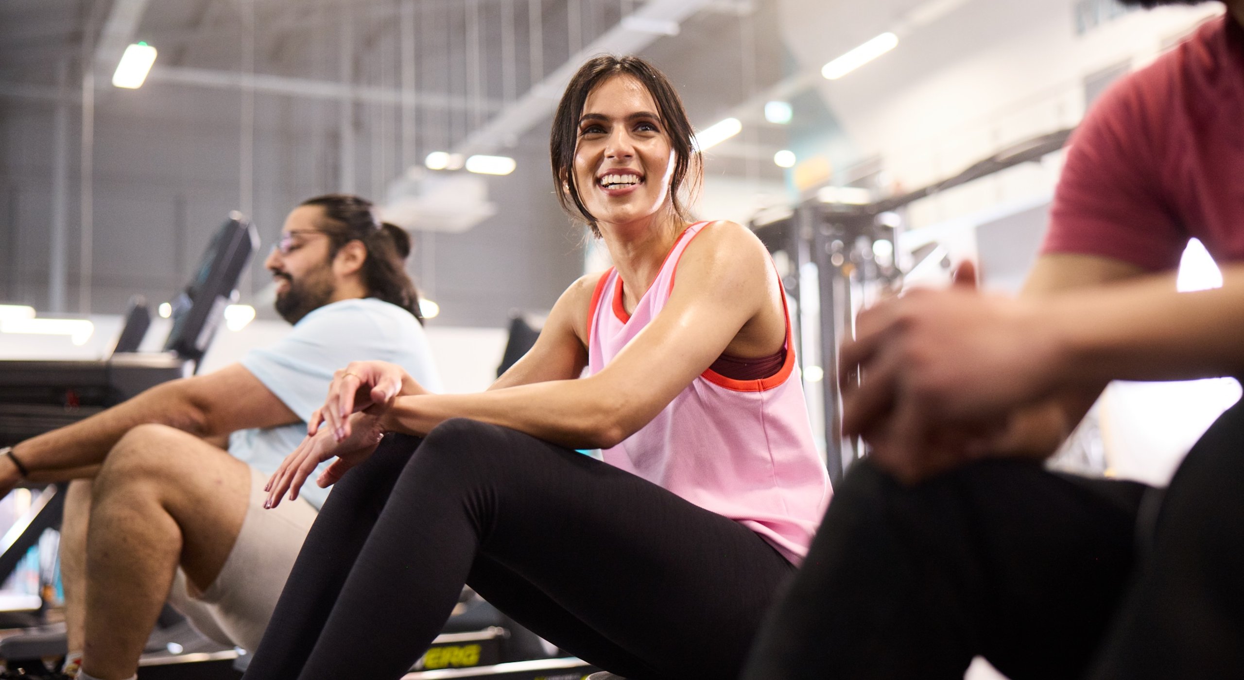 A woman smiles while seated on a rowing machine, showcasing a positive workout experience.
