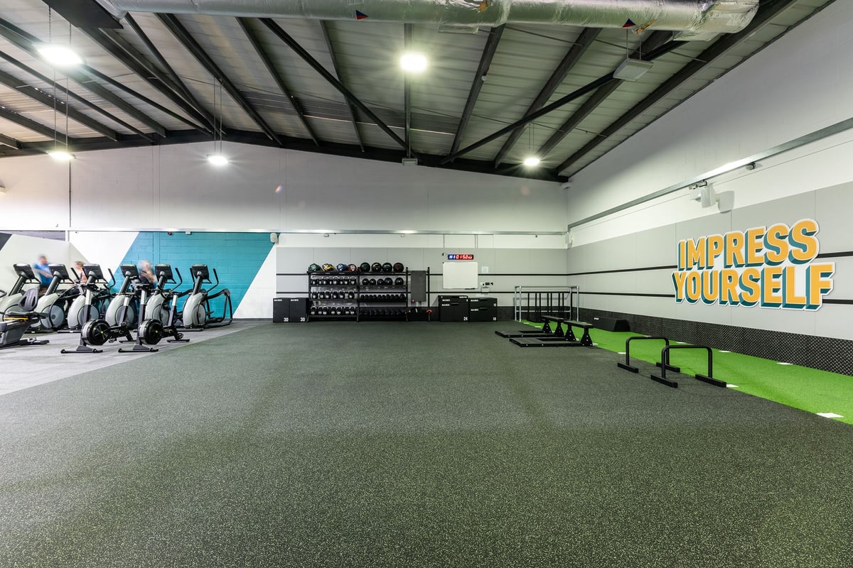 PureGym Lincoln St Marks Centre: Weightlifting area with benches, dumbbell racks, wall mural, and green rubberized flooring.