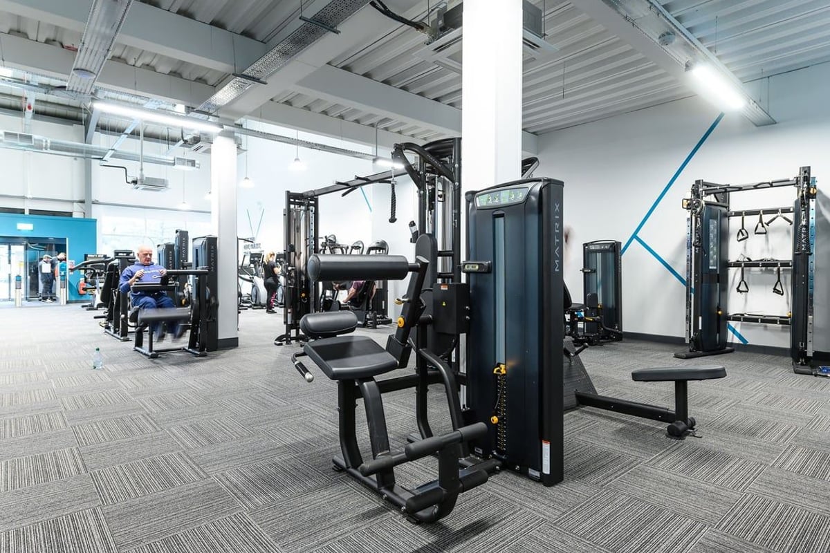 PureGym Glossop: Rows of strength training machines, benches, weight stacks, and rubberised flooring within a gym facility.