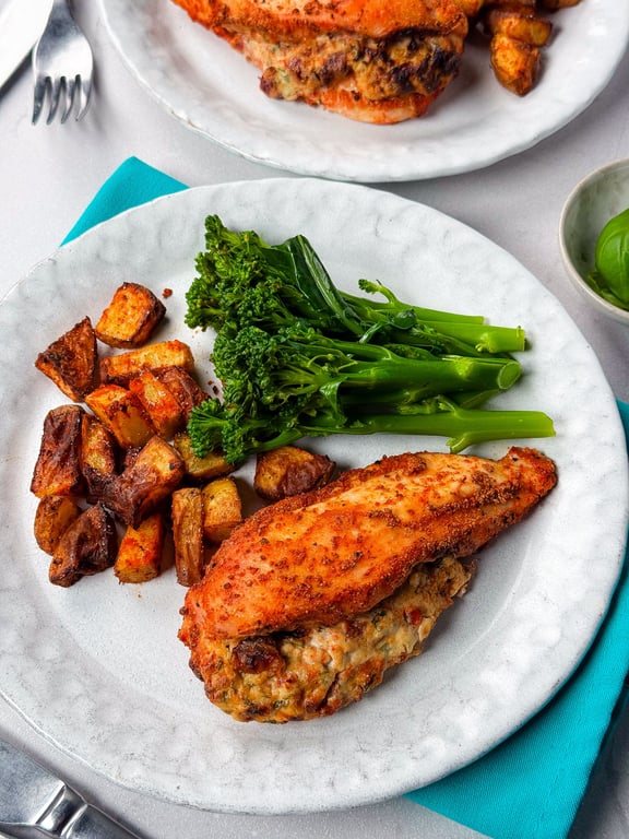 Stuffed chicken breast with roasted potatoes and steamed broccolini on a white plate