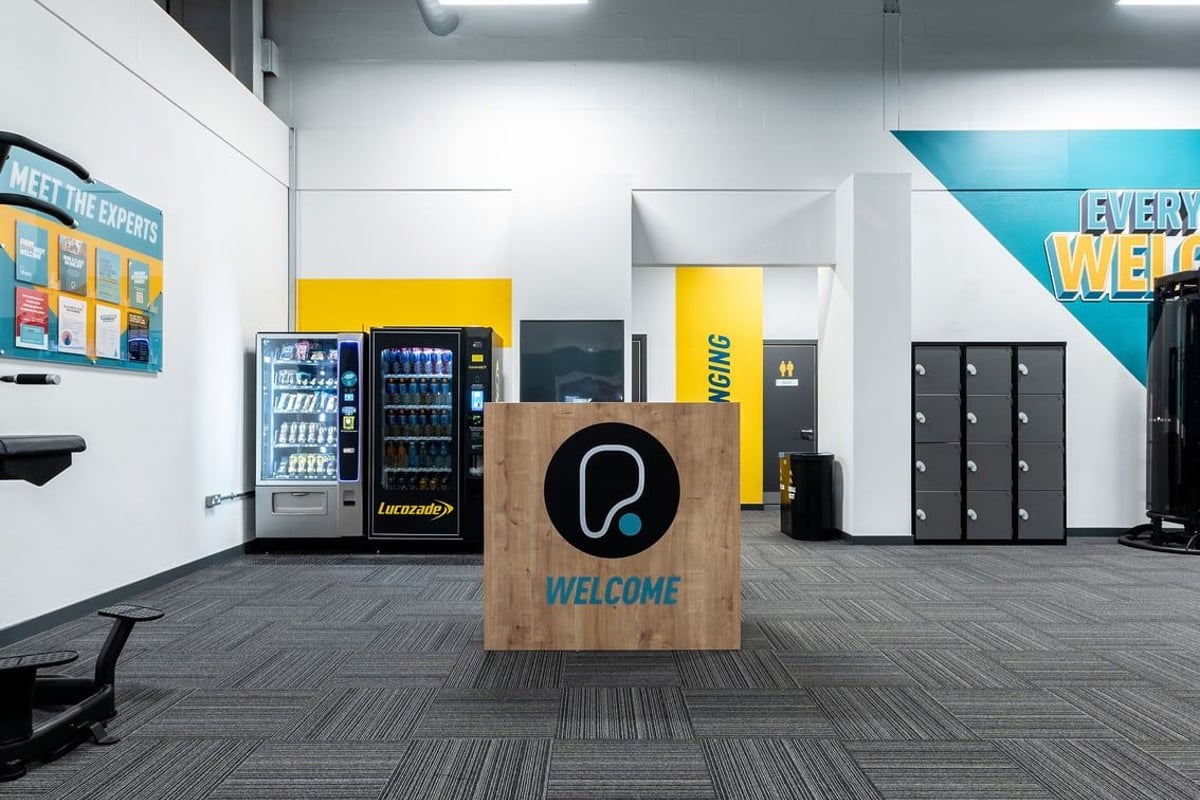 PureGym Uttoxeter: Vending machines, welcome sign, lockers, and tiled flooring in a gym lobby area.