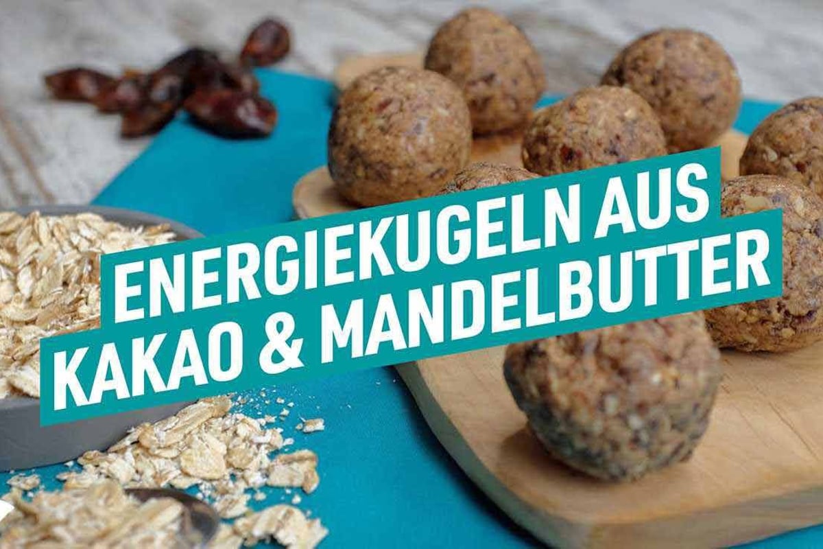Energiebällchen aus Kakao und Mandelbutter auf Holzbrett mit Haferflocken daneben