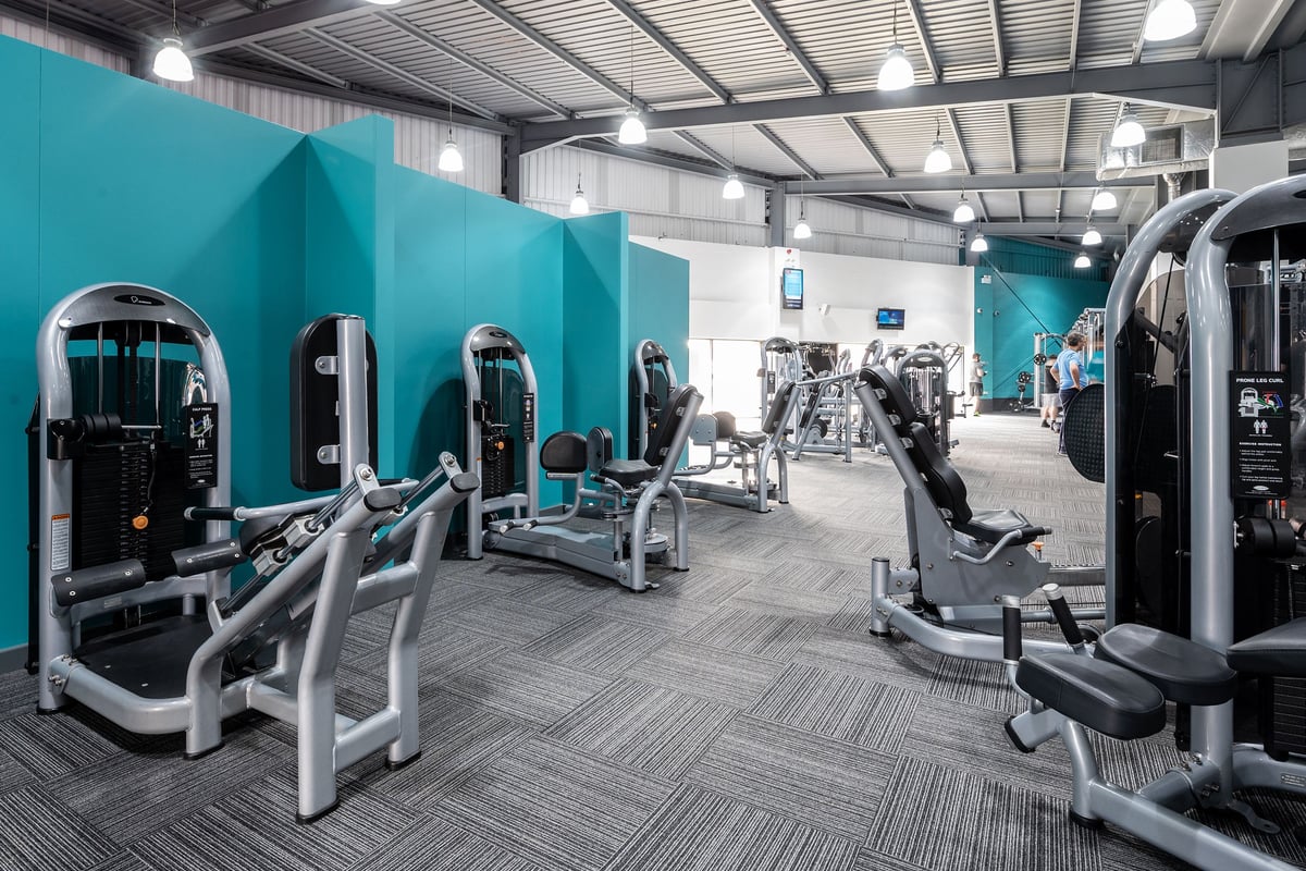 PureGym Warrington Central: Resistance machines, weight benches, and rubberized tiled flooring in a teal-colored gym studio.