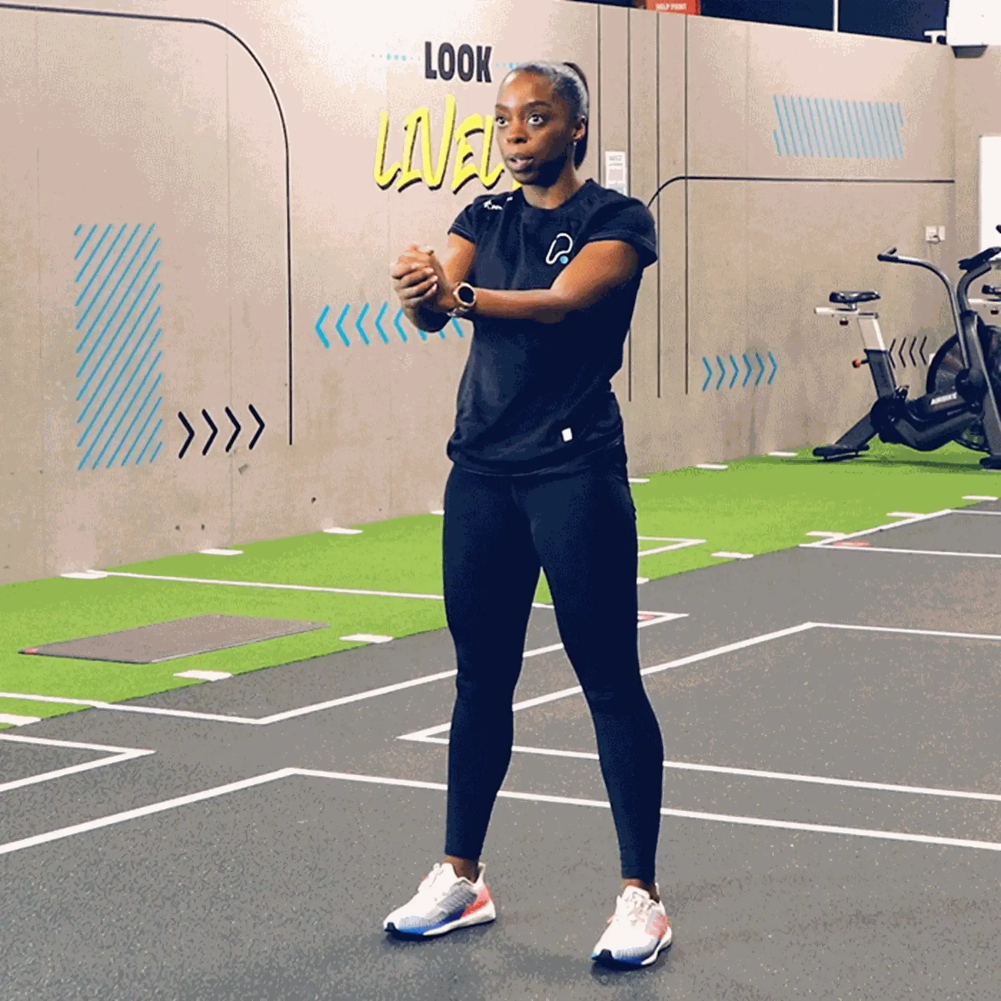 Woman in sportswear stretching arms in a gym with exercise bikes in the background
