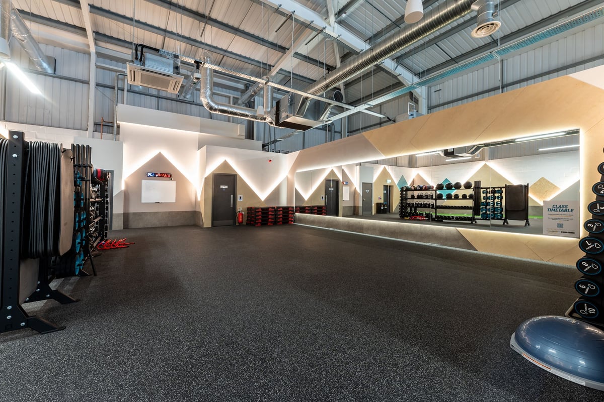 PureGym Spalding: Rubberized flooring, arched structures, shelves with equipment, curtained area.