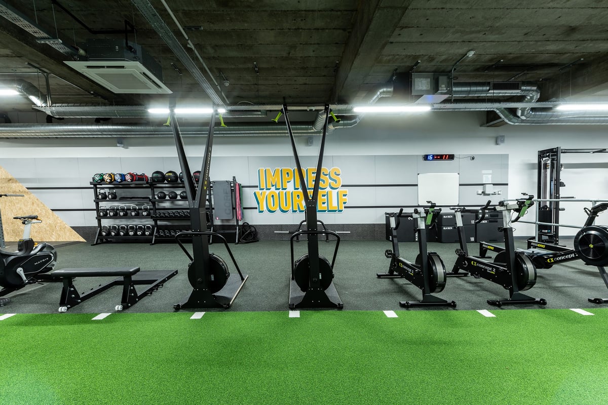 PureGym London Streatham: Gym studio with weight racks, suspended punching bags and rubberized green flooring.