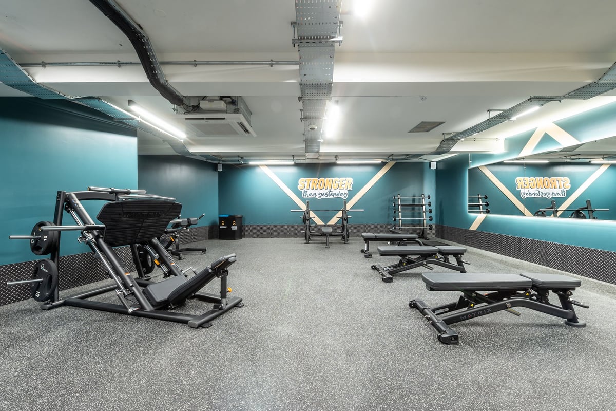 PureGym London Welling: Weight benches, squat racks, rubberized flooring in a teal and grey gym studio.