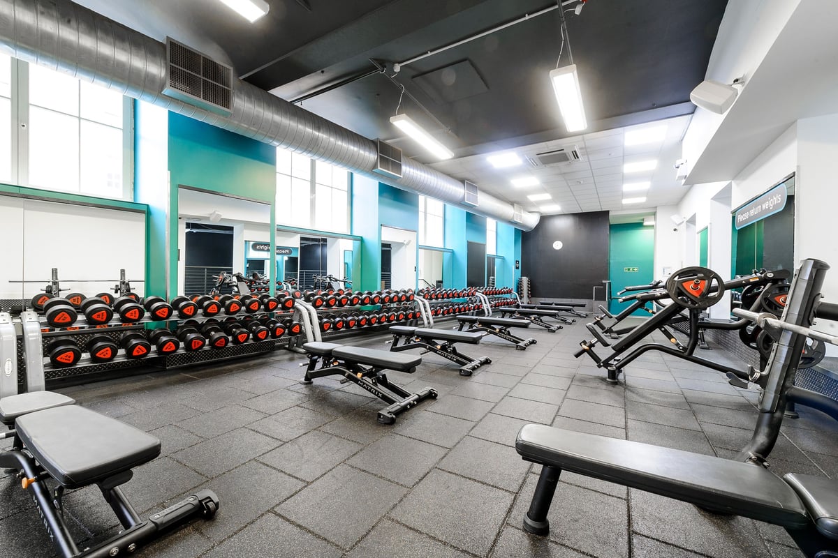PureGym Dundee: Rows of dumbbell racks, flat benches, resistance machines, and mats in a teal and grey gym studio.