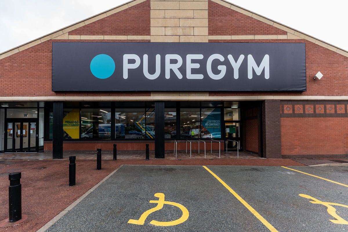PureGym Bangor Wales: The exterior of a gym franchise with a sign, parking spaces, and accessibility markings.