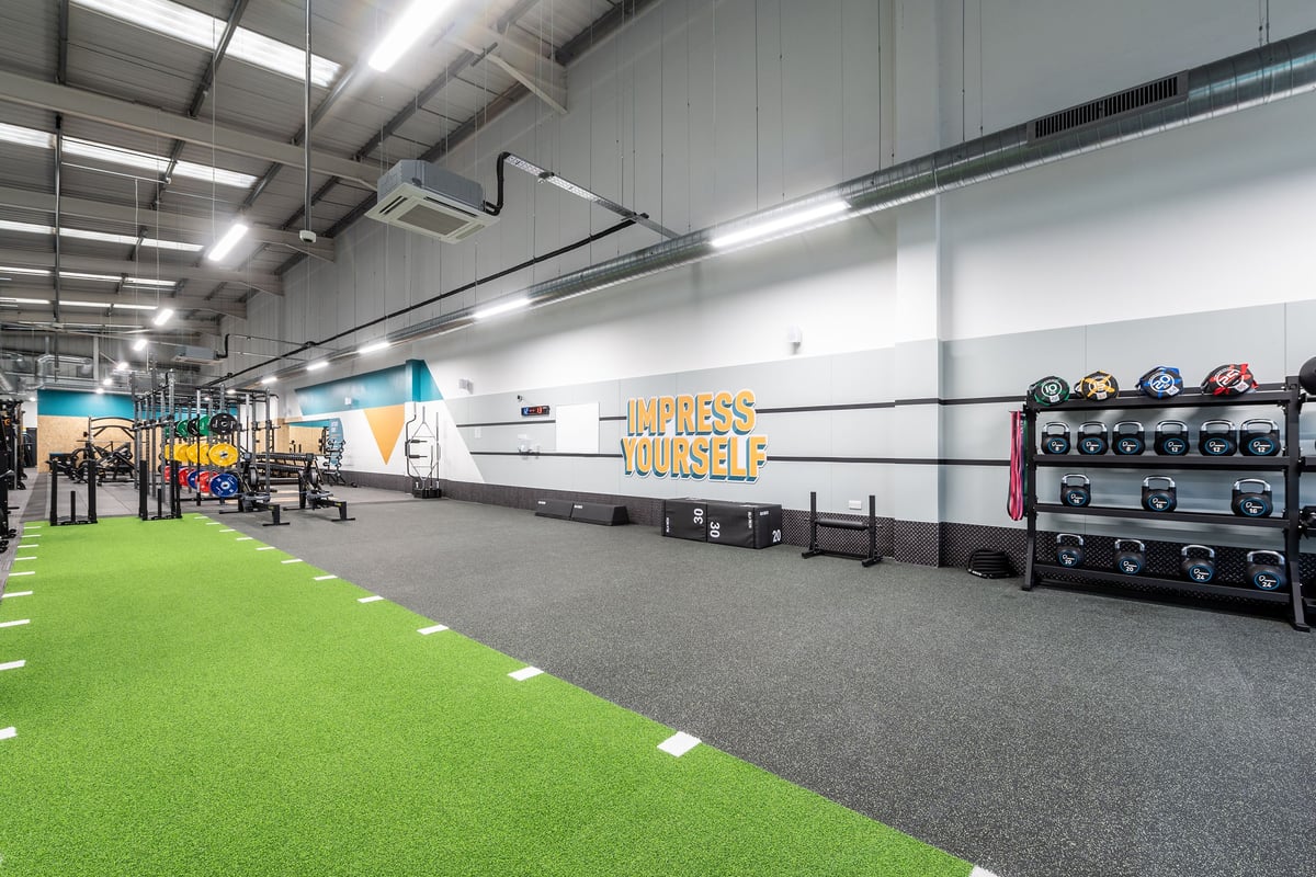 PureGym Newhaven: Green turf, weight racks, mirrored wall with motivational text, air ducts overhead.