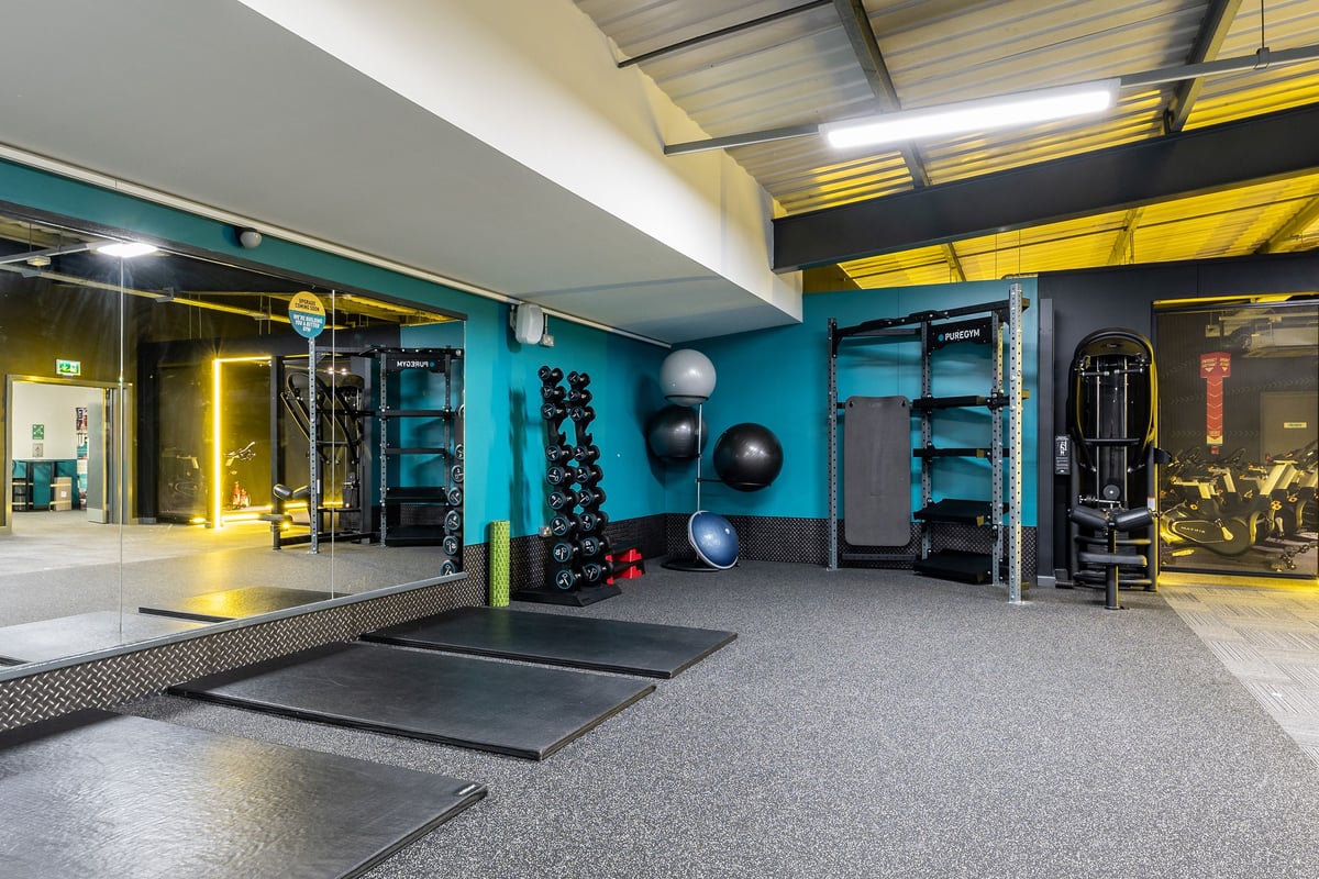 PureGym West Thurrock: Resistance training area with weight racks, medicine balls, rubberized floors, and teal accent walls.