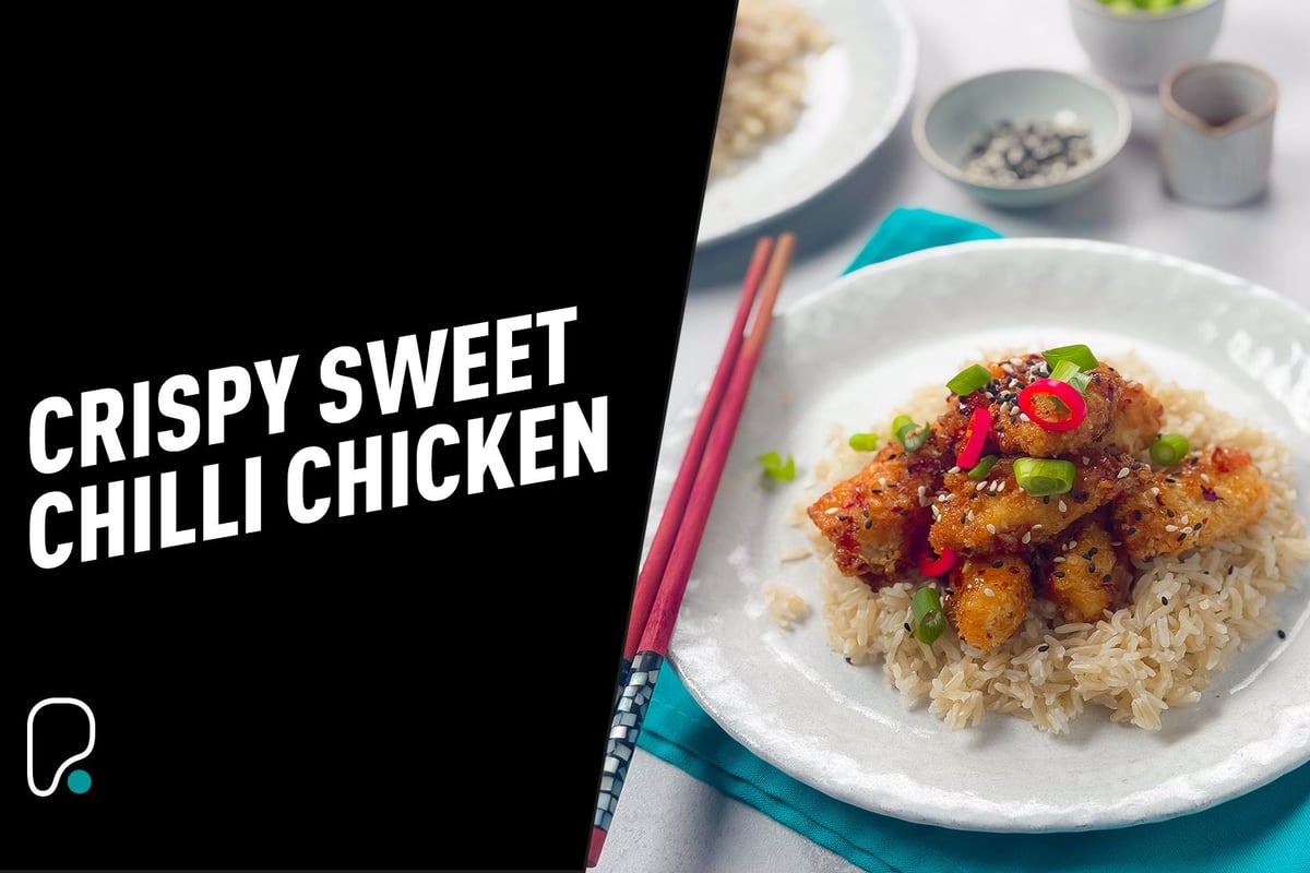 Crispy sweet chilli chicken on rice garnished with spring onions and red chillies.