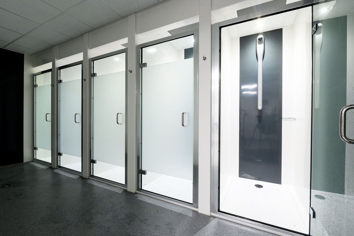PureGym Bristol Abbey Wood Retail Park: Glass-fronted shower cubicles with metal framing in a tiled changing room.