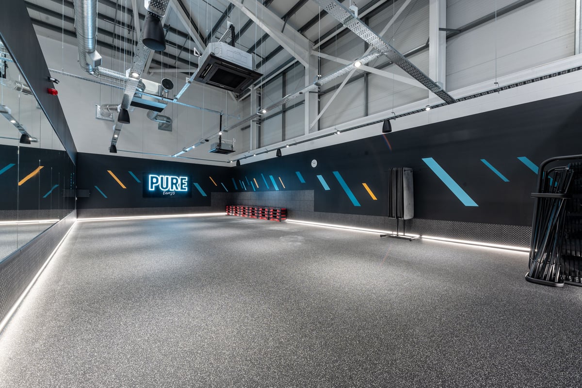 PureGym Port Talbot: Rubberized flooring, neon lighting along walls, appears to be an indoor functional training area.