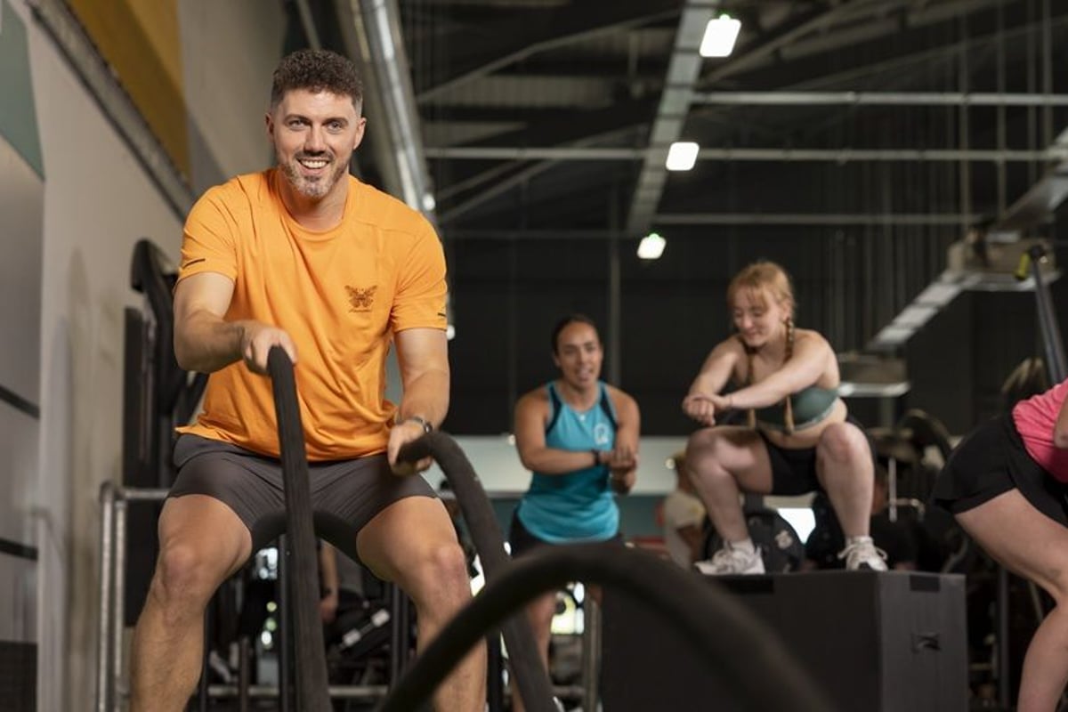 Man in orange t-shirt on exercise bike with three people exercising in background