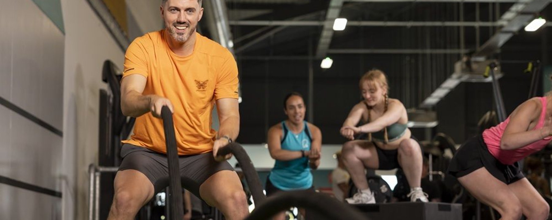 Man in orange t-shirt on exercise bike with three people exercising in background