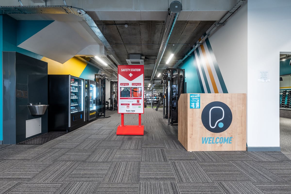 PureGym Brentwood: Vending machines, benches, mirrors along walls, rubberized flooring in a commercial gym setting.