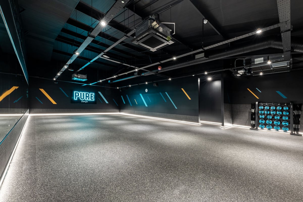 PureGym Crewe Grand Junction Retail Park: Mirrored studio space with atmospheric lighting and weight plates along the wall.