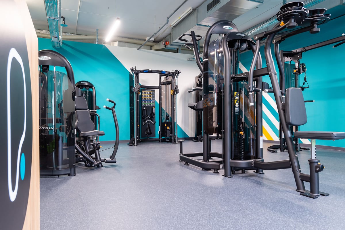 PureGym Wil: Studio de sport avec appareils de résistance, passe-câbles, bancs et touches de couleur bleu sarcelle partout.