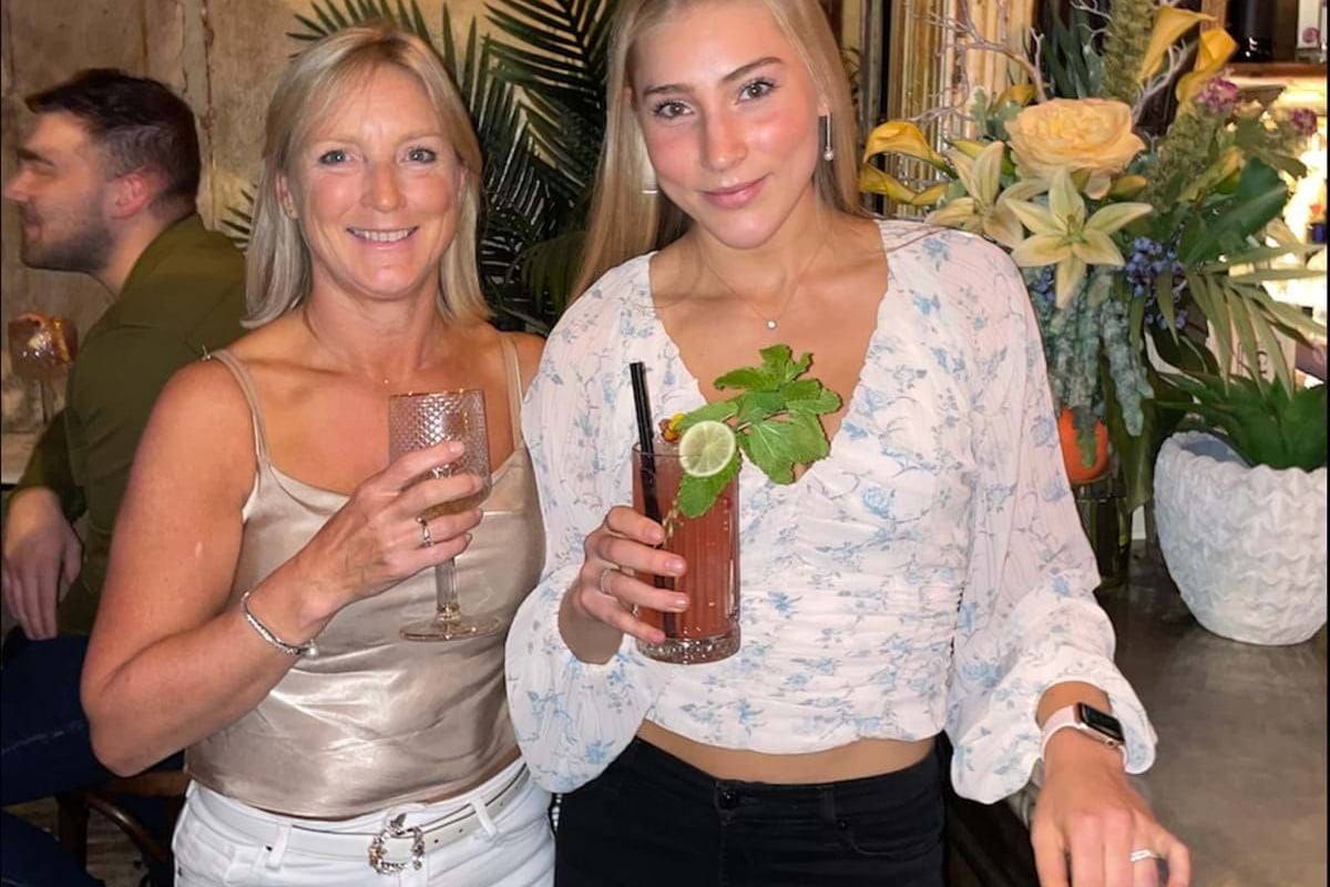 Two women holding drinks with floral decorations behind them