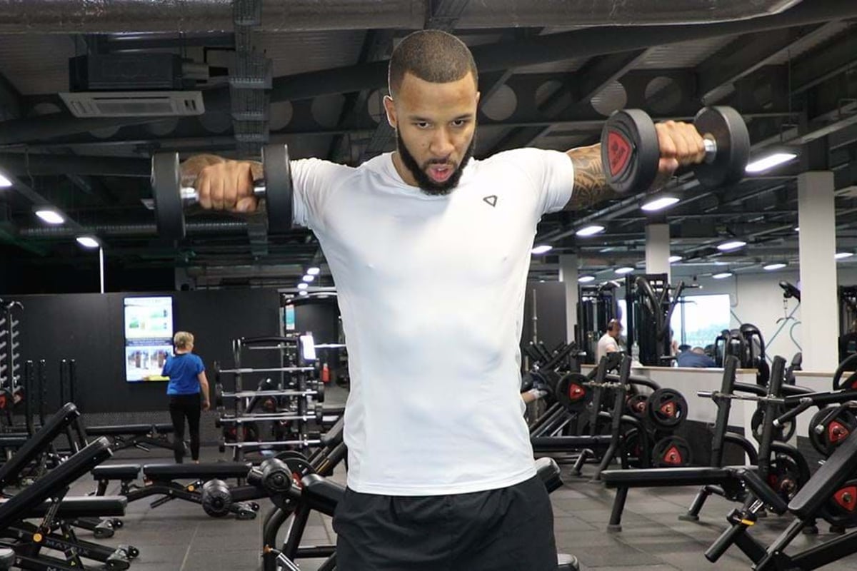 Man lifting dumbbells in a gym with exercise equipment in the background
