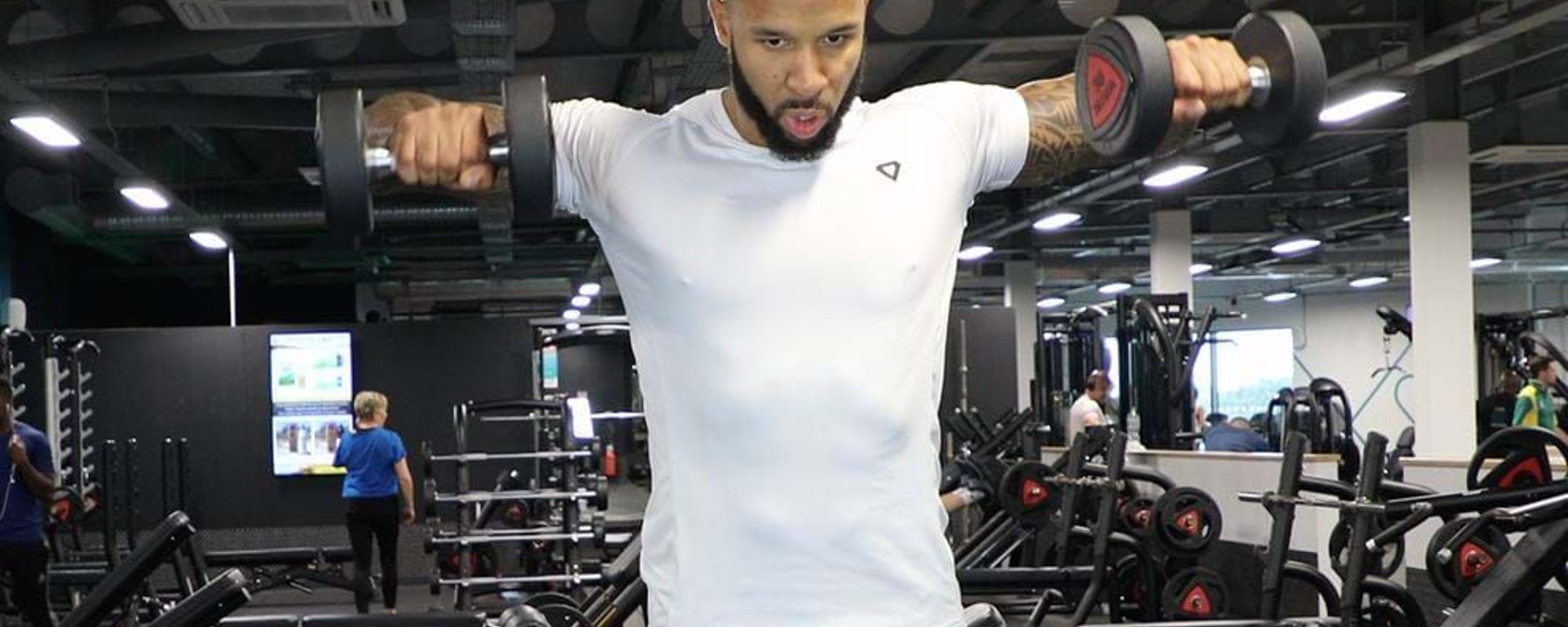 Man lifting dumbbells in a gym with exercise equipment in the background