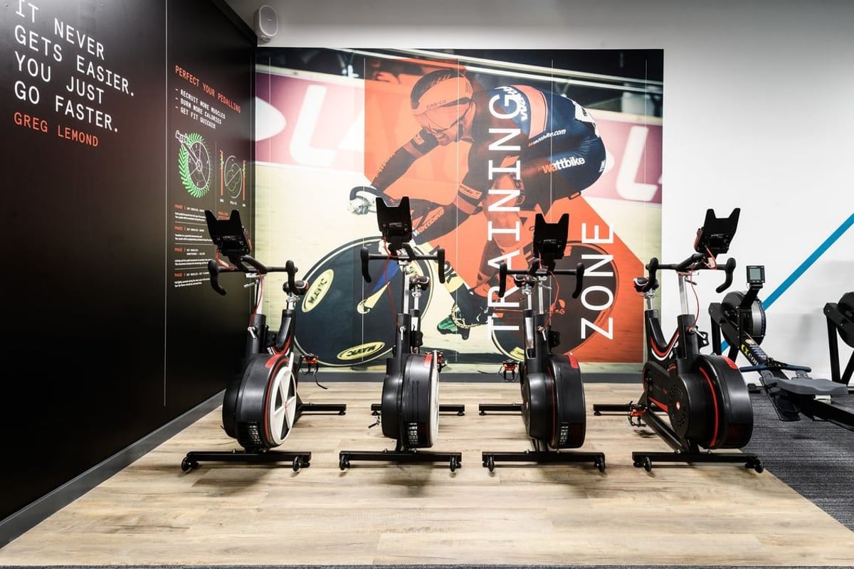 PureGym East Grinstead: Rows of exercise bikes, dumbbells on floor, motivational poster in background.