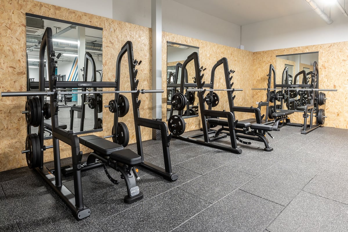 PureGym Torquay Bridge Retail Park: Rows of squat racks with weight plates and benches in a wood-panelled room.