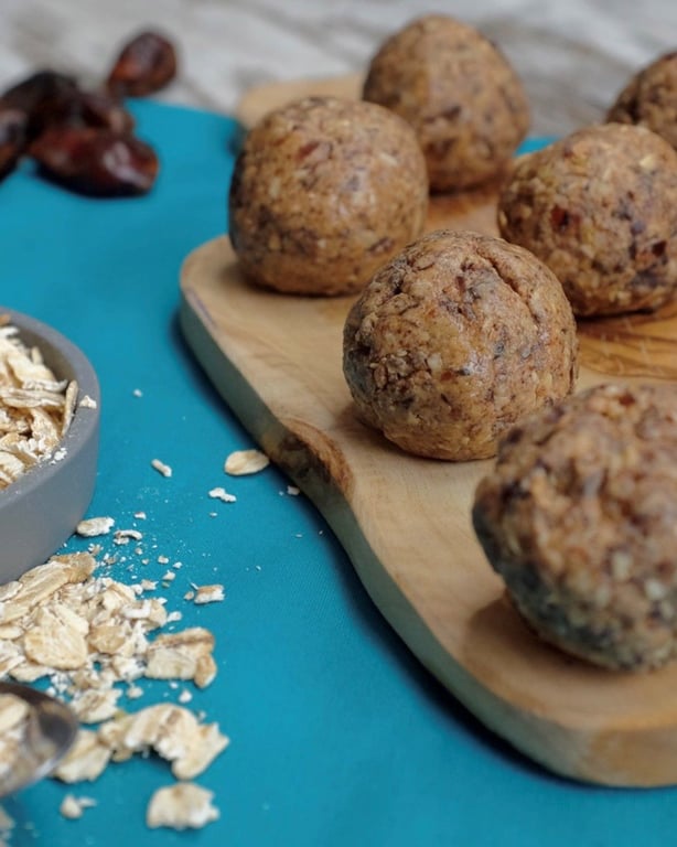 Energy balls on a wooden board with oats and dates on a blue surface nearby